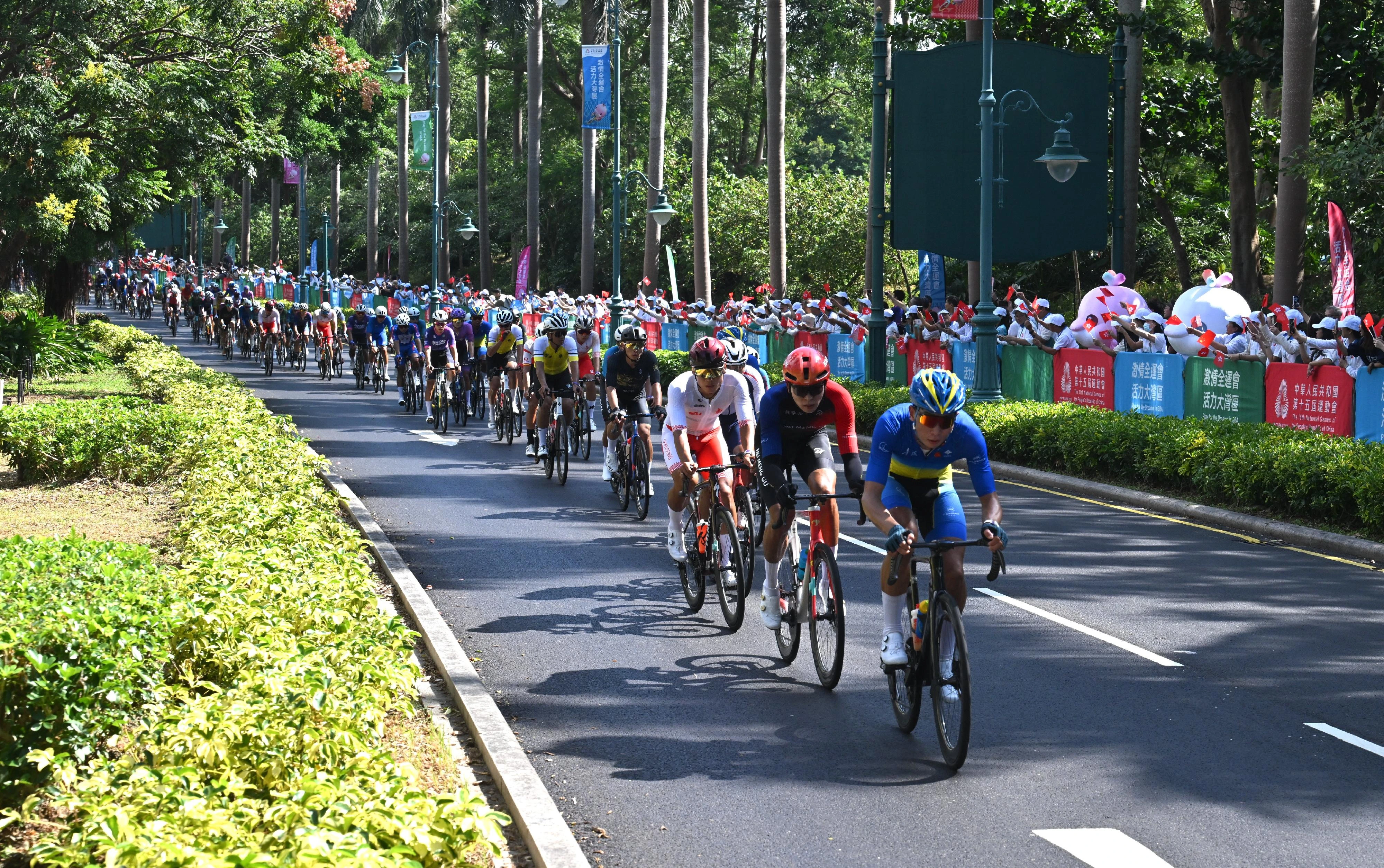 第十五届全国运动会「中国移动盃」自行车（公路）比赛的男子个人赛十一月八日在珠海、香港、澳门三地城市道路和港珠澳大桥举行。图示参赛选手在香港迪士尼乐园度假区附近赛道作赛，市民在路旁为选手打气。